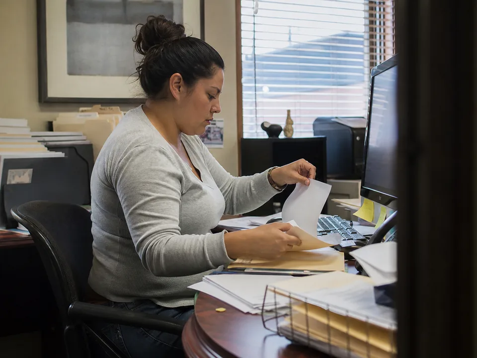 Paralegal sorting client pay stubs and bank statements into folders beside a computer at a small bankruptcy law office