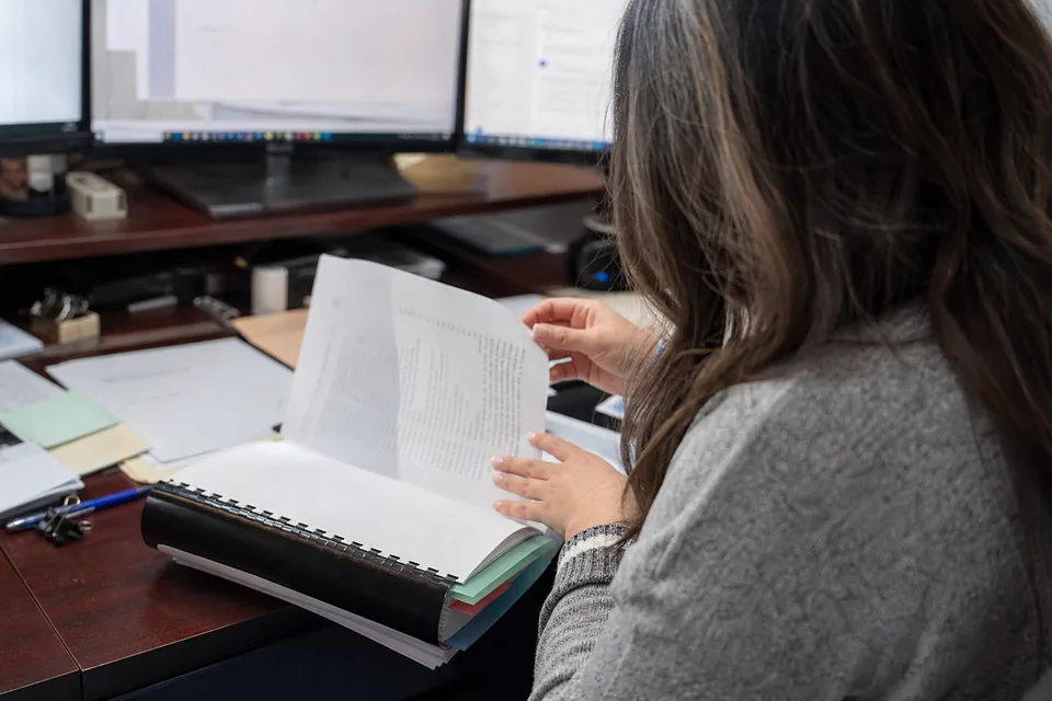 Paralegal seen from behind assembling a bound appellate brief with a printed table of authorities and tabbed binder