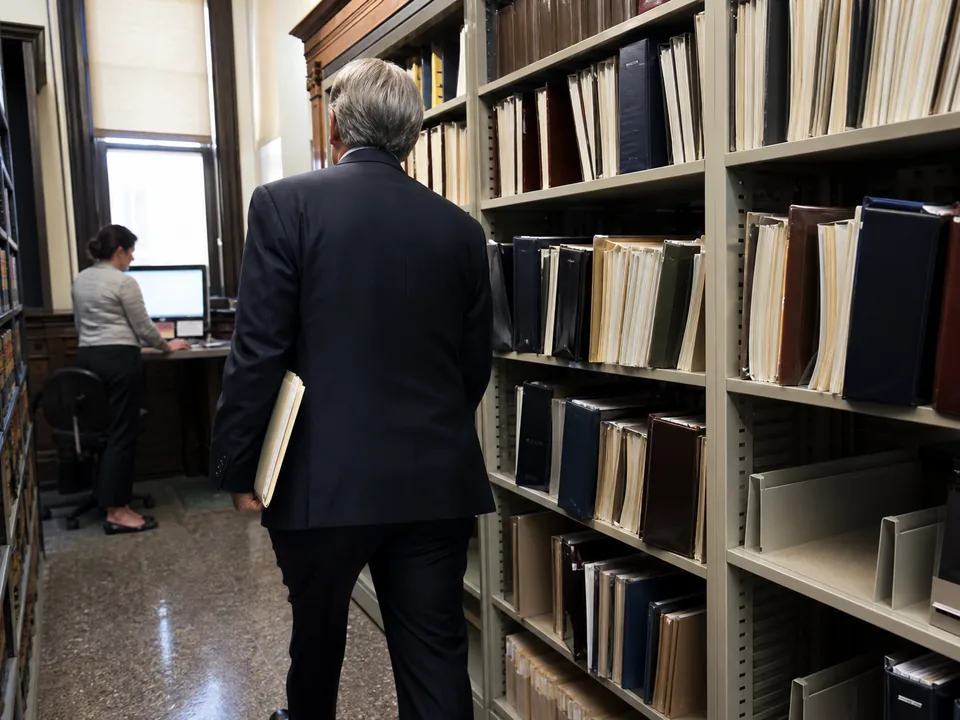Attorney walking down a courthouse law library aisle of loose-leaf treatises toward a public research terminal